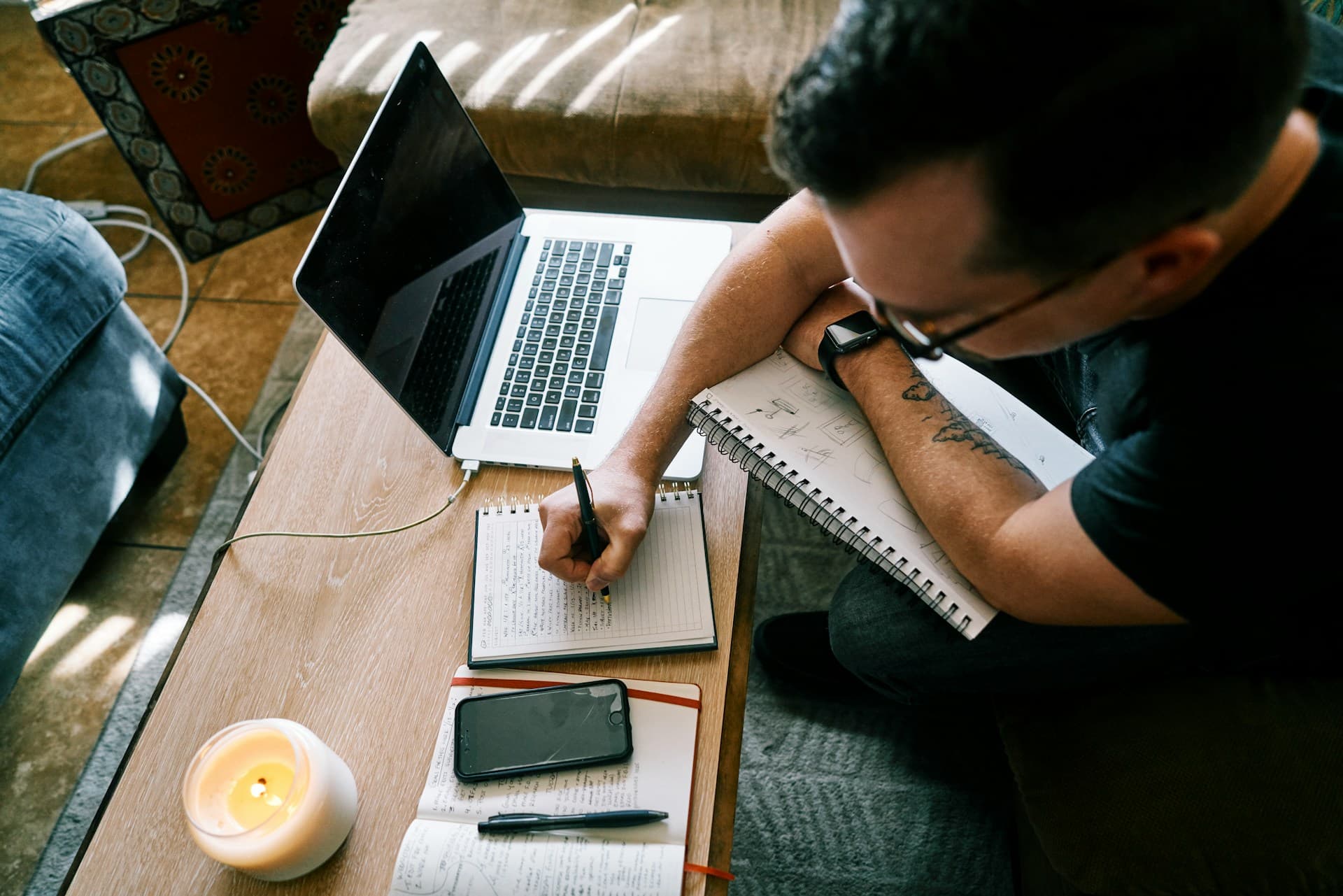 Pessoa escrevendo anotações num caderno ao lado de um notebook, vista de cima